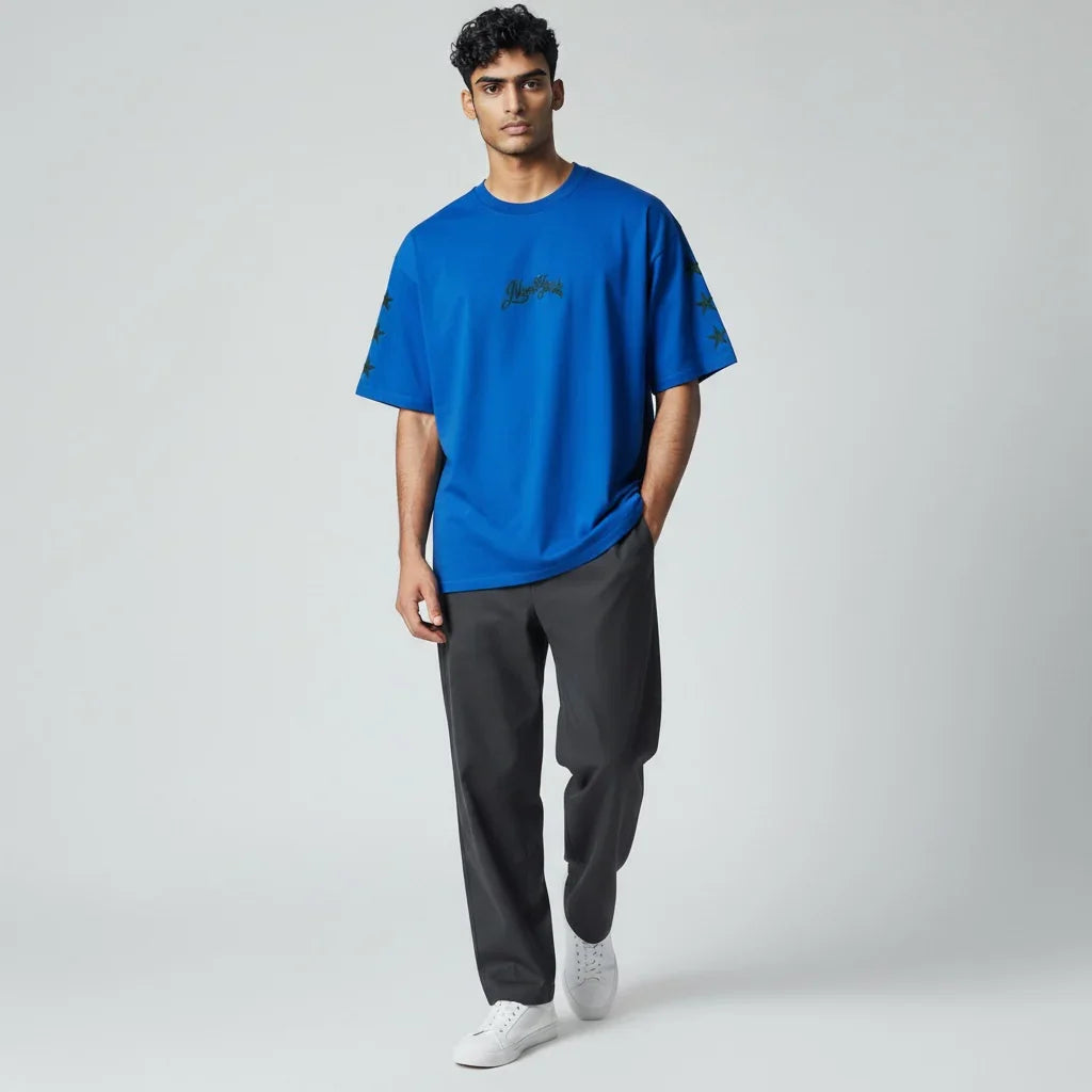 Man wearing oversized blue graphic t-shirt with black stars, gray pants, and white sneakers