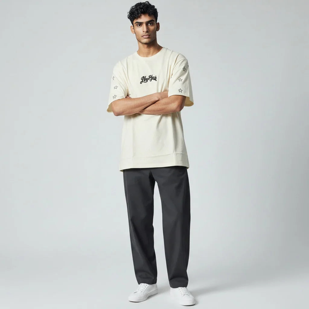 Man wearing beige graphic t-shirt with star details, black pants, and white sneakers