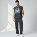 Man wearing sleeveless black shirt with bold white spider graphic, gray pants, and white sneakers