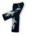 Black streetwear pants with bold white tribal graphic print, flat lay on white background