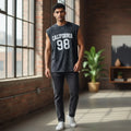 Man in sleeveless black California 98 graphic shirt and dark jeans, casual modern indoor setting