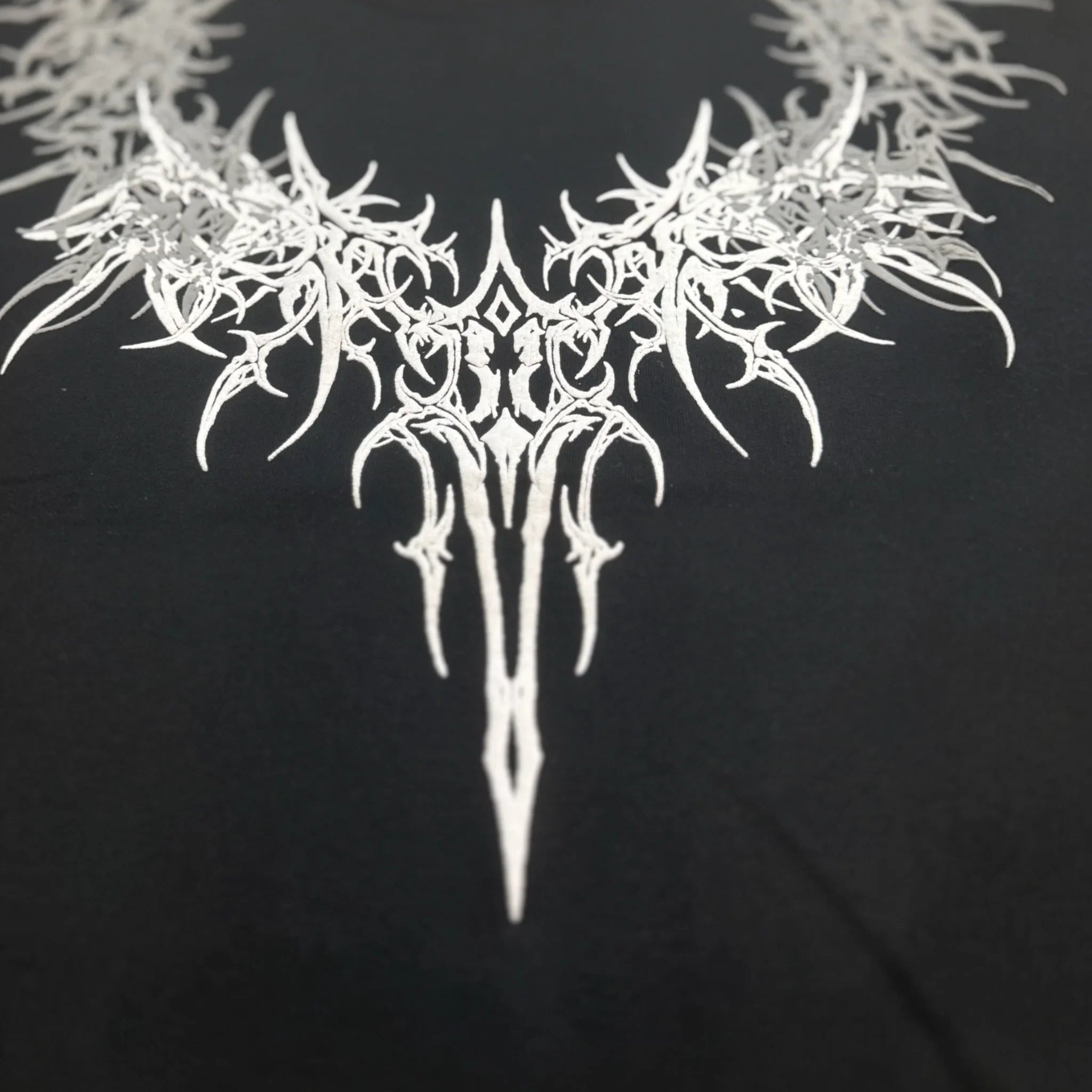 Black shirt with intricate white tribal graphic barbed design on the chest