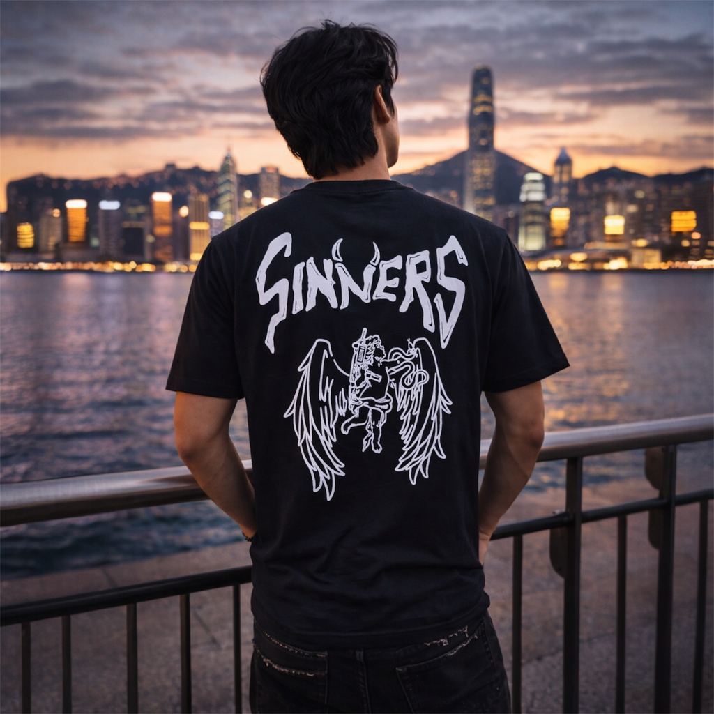Man in black graphic SINNERS t-shirt with angel print, city skyline at sunset background